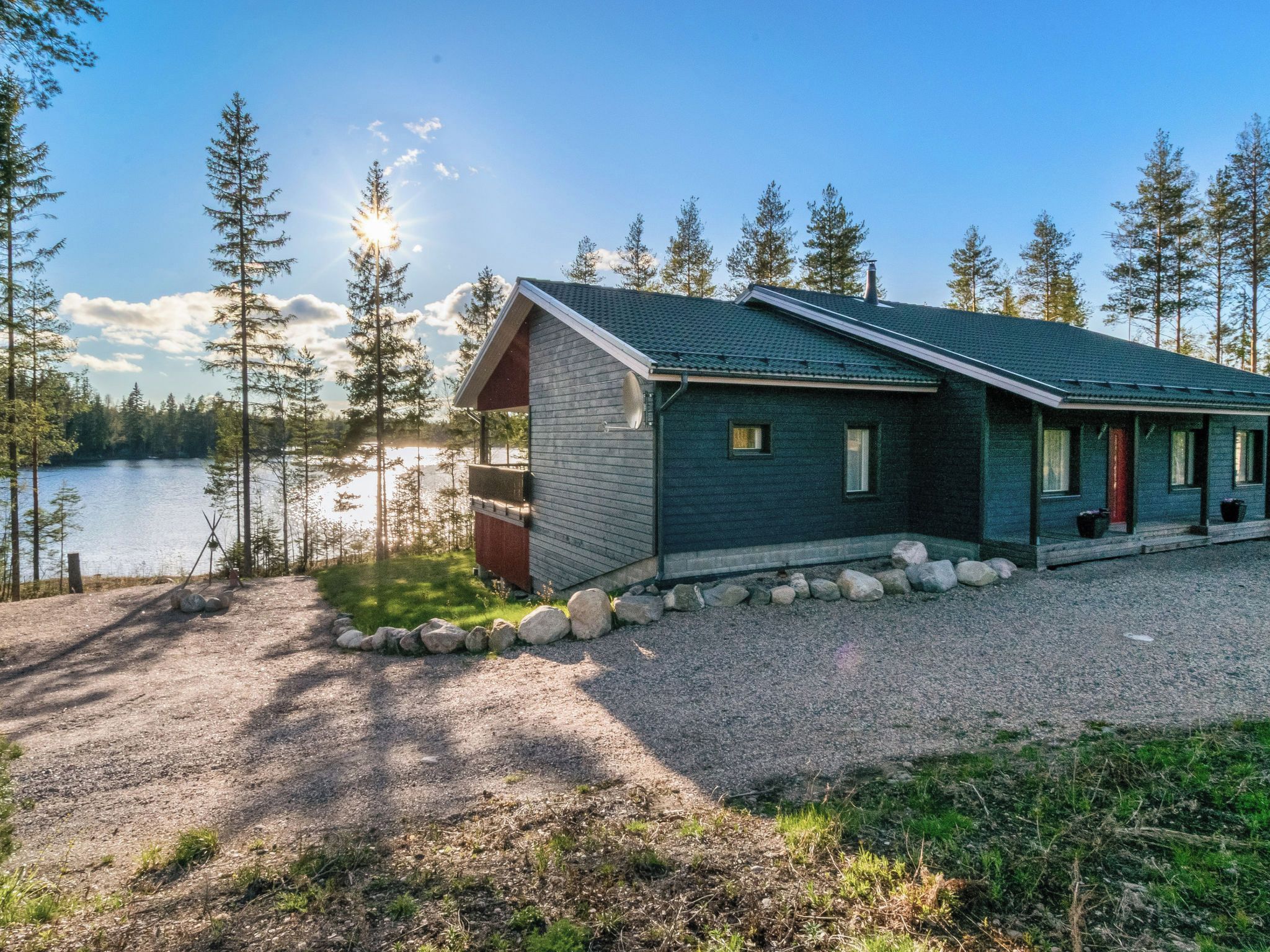 A cabin with a gravel driveway, surrounded by trees and a lake.
