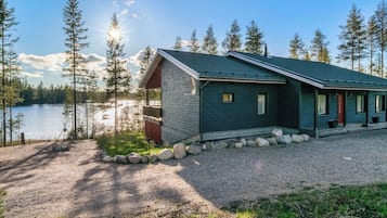 A cabin with a gravel driveway, surrounded by trees and a lake.