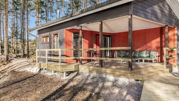 Una baita con una terrazza in legno, un'area salotto esterna coperta e vista su una foresta.