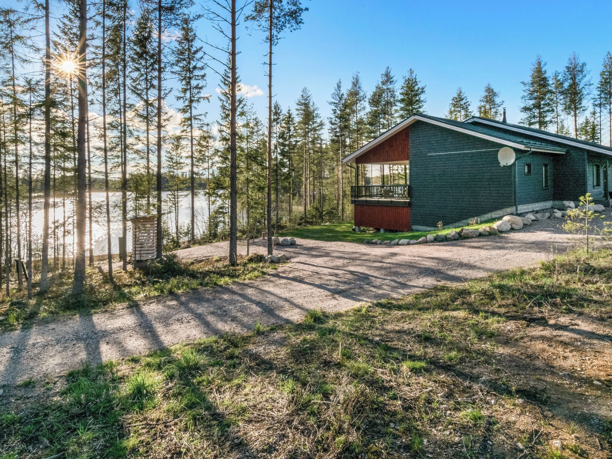 A cabin with a deck, surrounded by a forest and a lake.