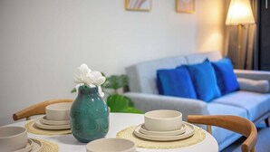 A dining table set with plates, bowls, and a vase with flowers. A sofa with blue cushions is in the background.
