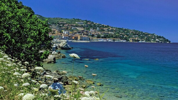 Un pueblo costero con aguas azul cristalino, costa rocosa y abundante vegetación.