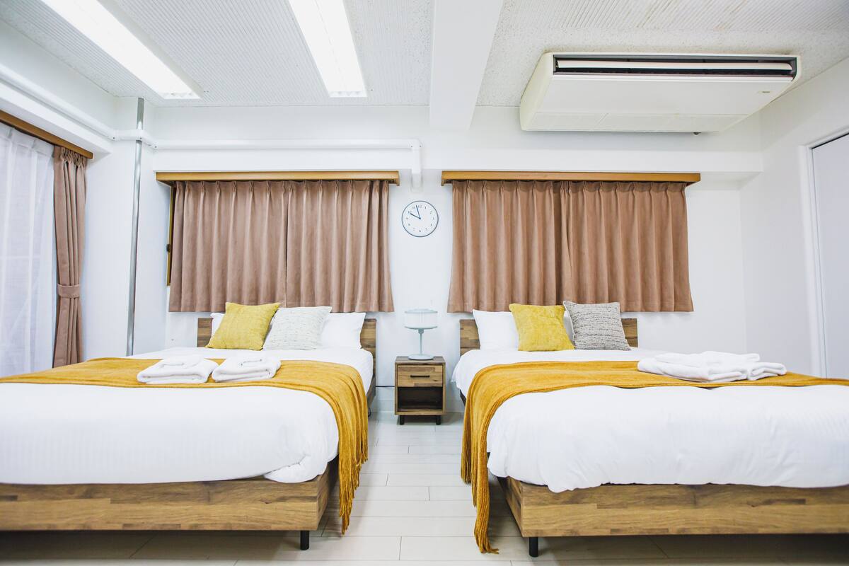 A hotel room with two beds, a clock, an air conditioner, and a small table between the beds.