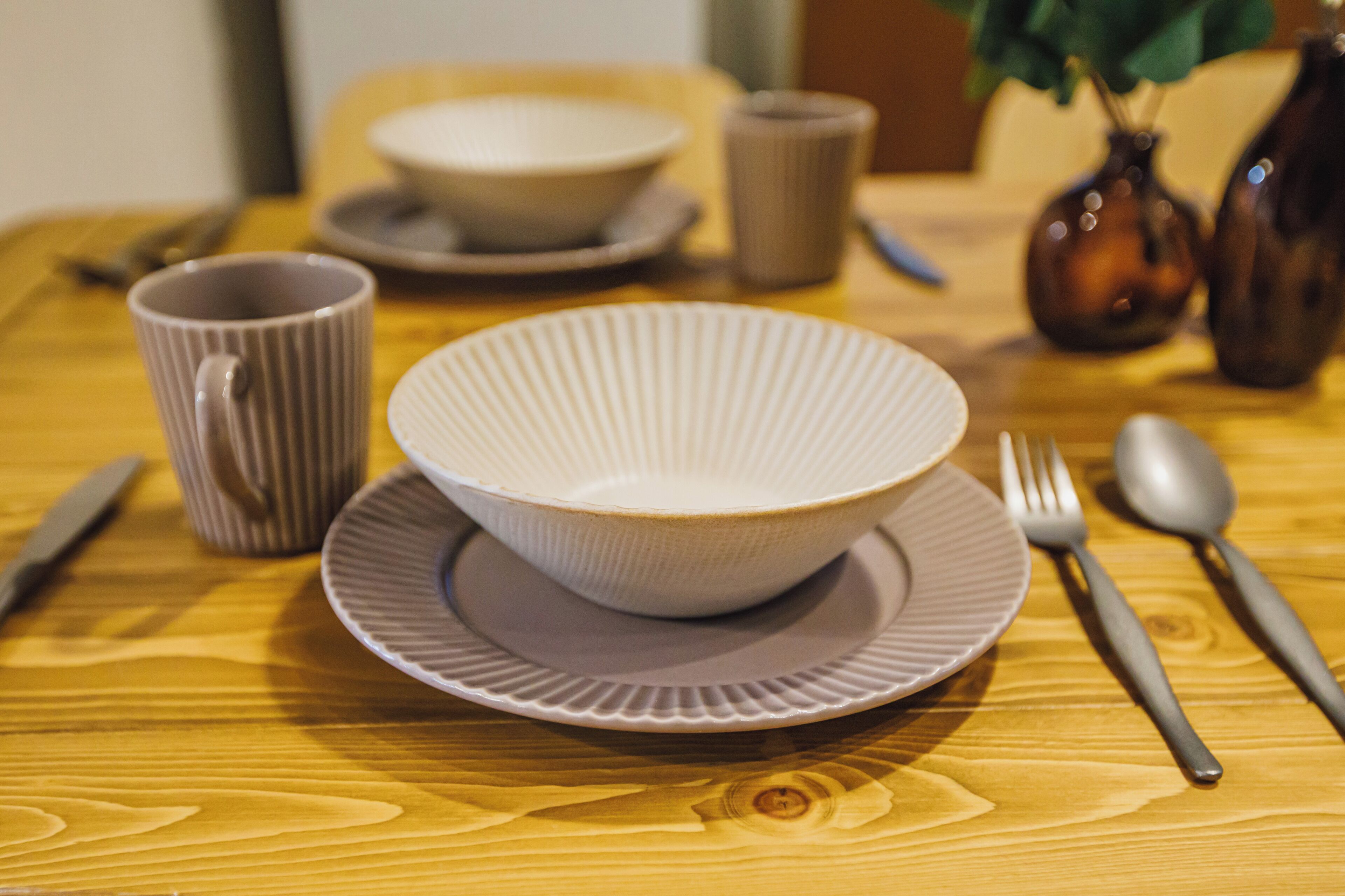 Une table à manger avec un saladier, des assiettes, des couverts et un vase.