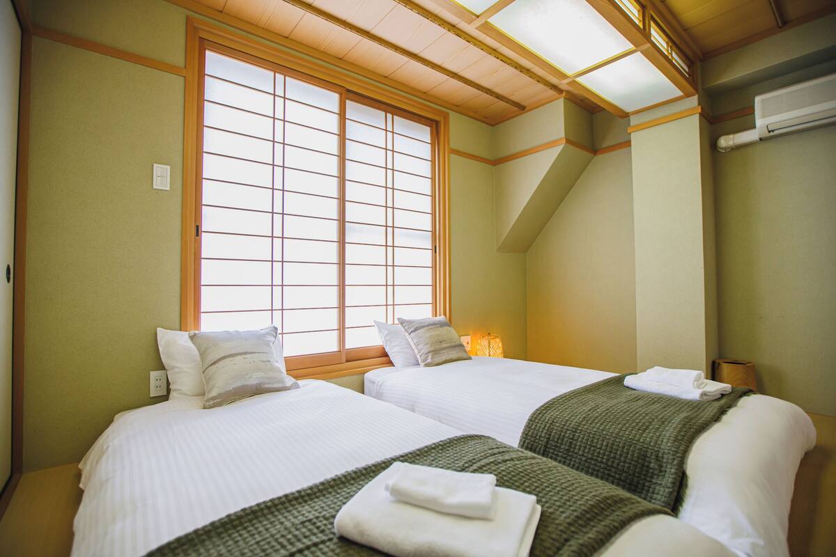 A hotel room with two beds, a large window with wooden frames, and a skylight.