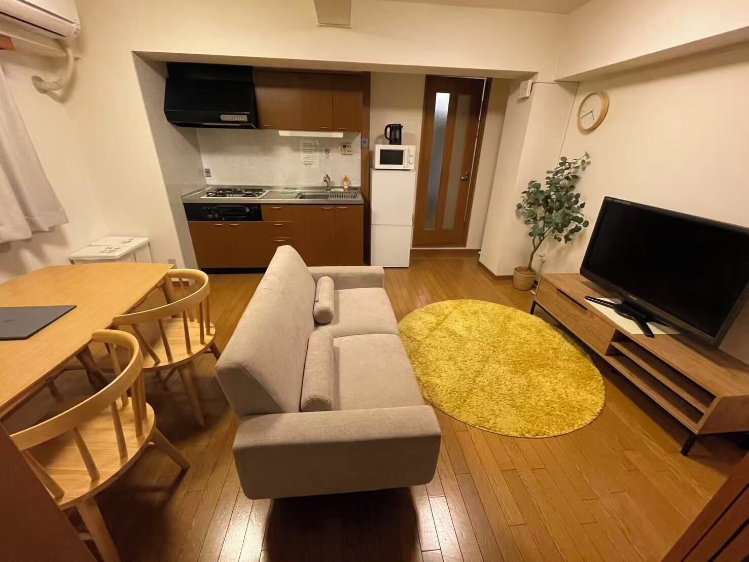 Un espacio habitable compacto con kitchenette, sofá, mesa de comedor, sillas y televisor.