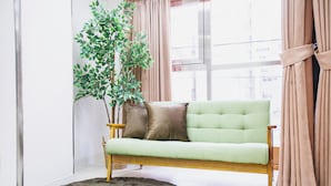 A green sofa with wooden legs and two cushions, a round rug, and a large potted plant. - R Residence Tanimachi (Osaka)
