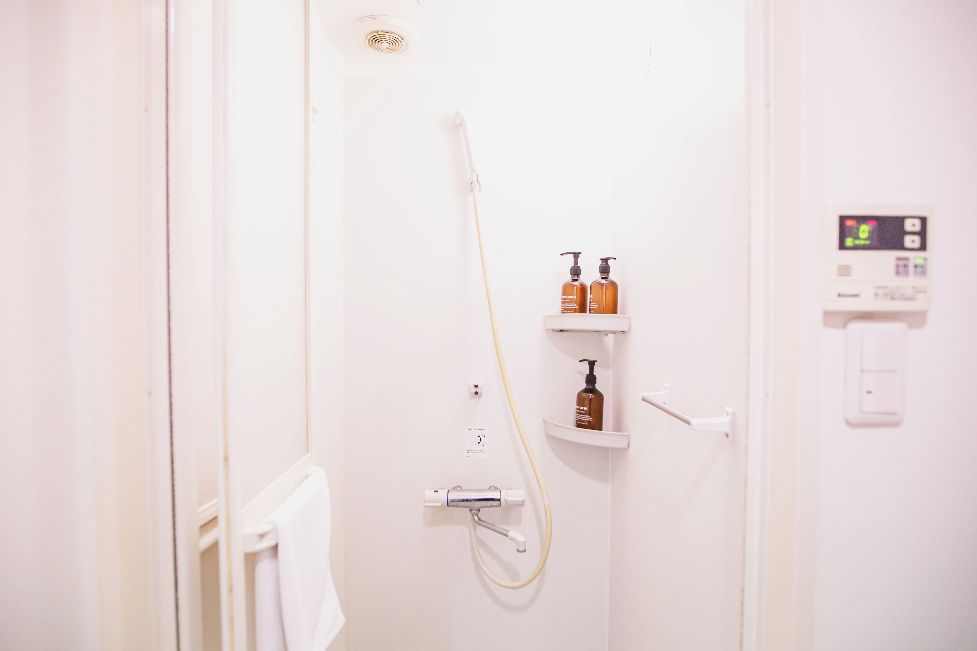 A bathroom with a shower, a towel rack, a soap dispenser, and a control panel.