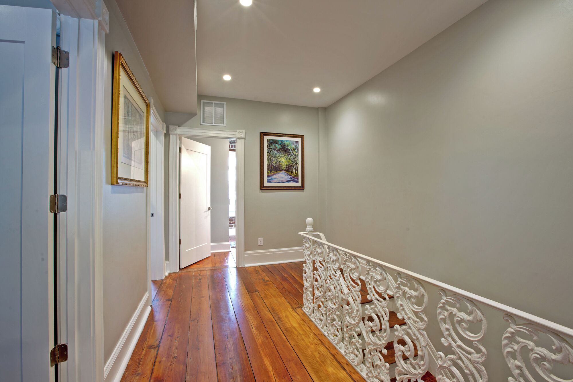A hallway with wooden flooring, white walls, and a white railing with ornate designs.