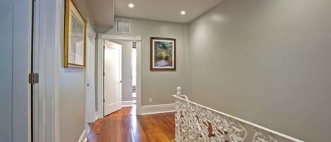 A hallway with wooden flooring, white walls, and a white railing with ornate designs.