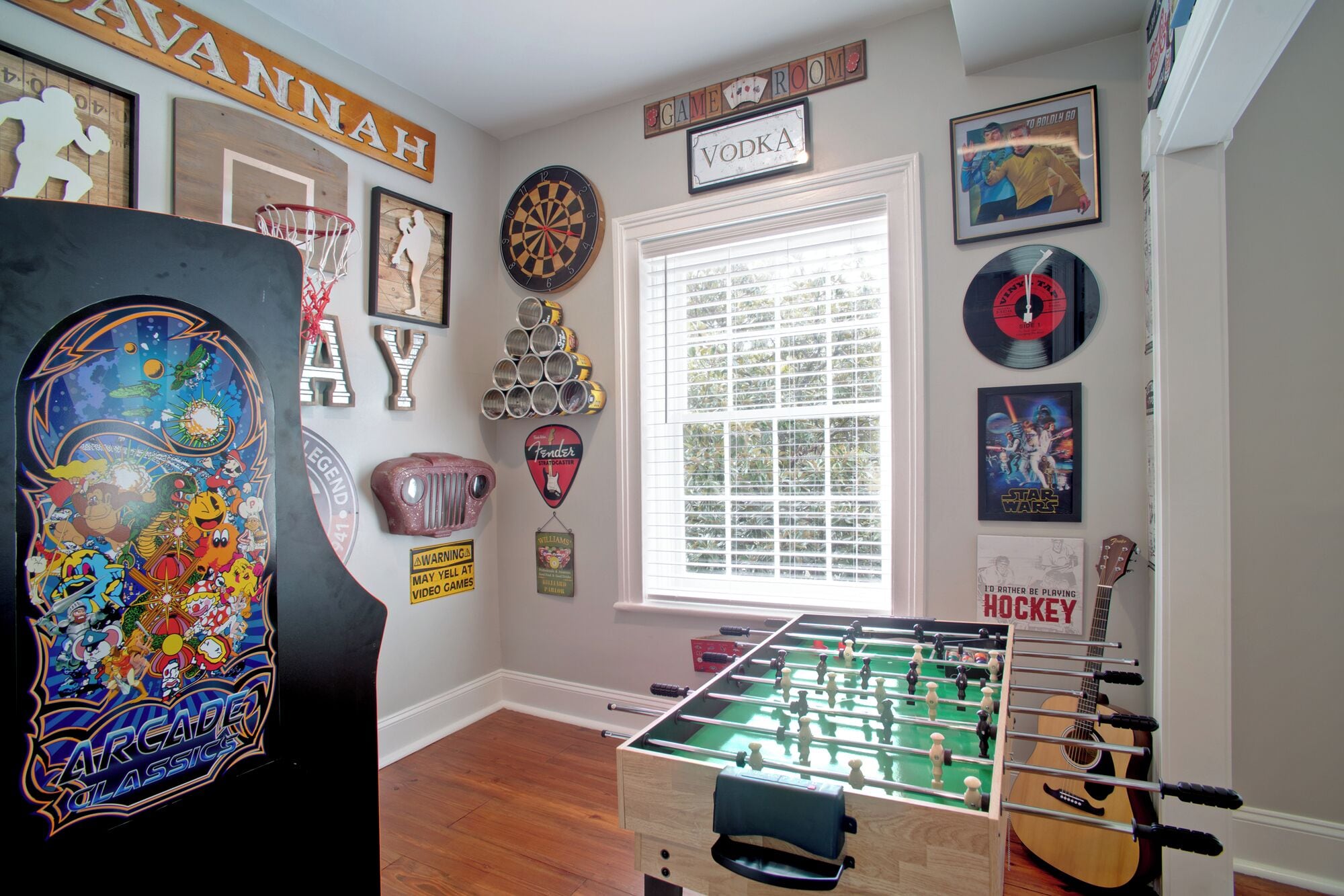 A room with a foosball table, arcade game, and various posters and memorabilia.