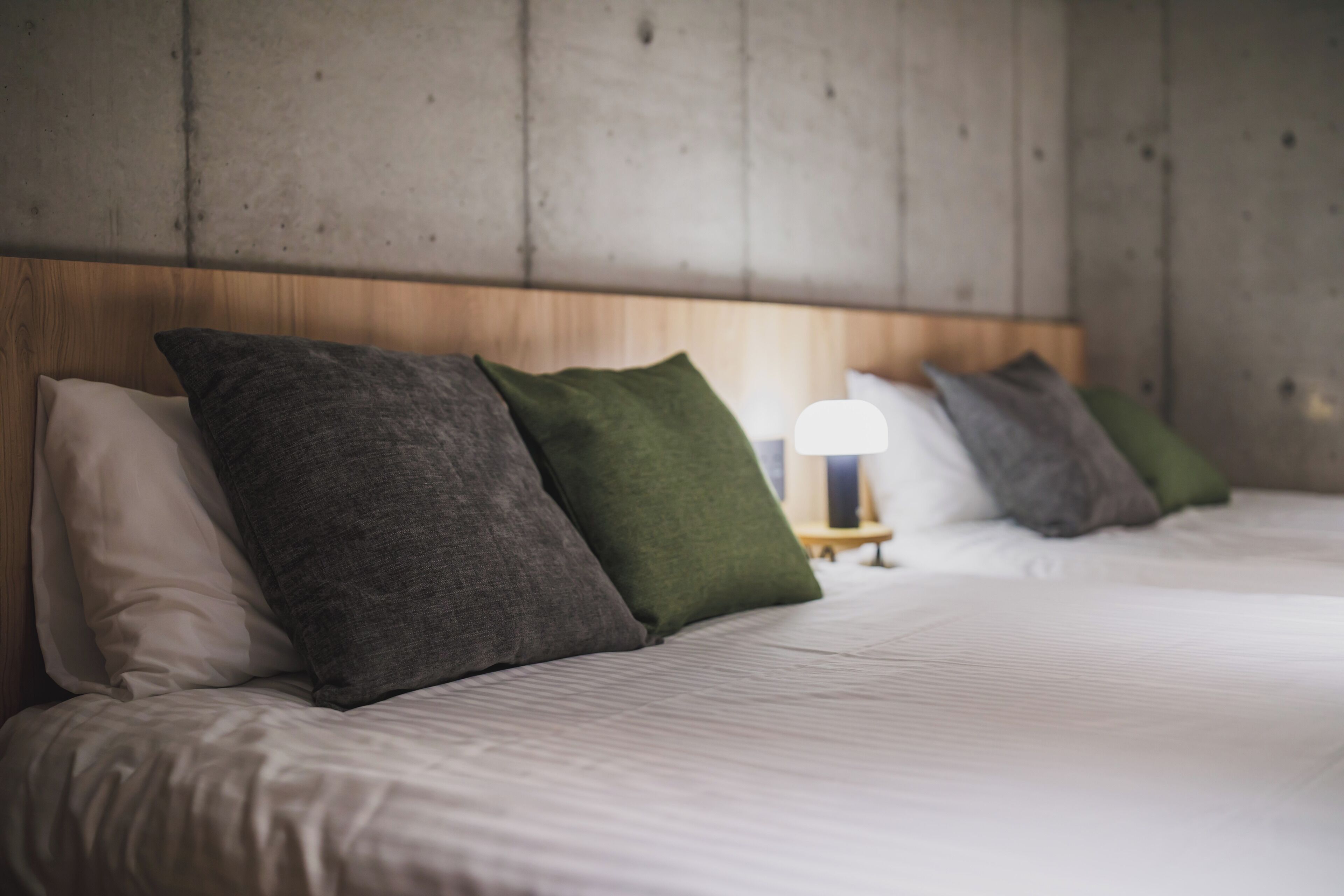 A hotel room with a wooden headboard, a bed with white linens, and a bedside table with a lamp.