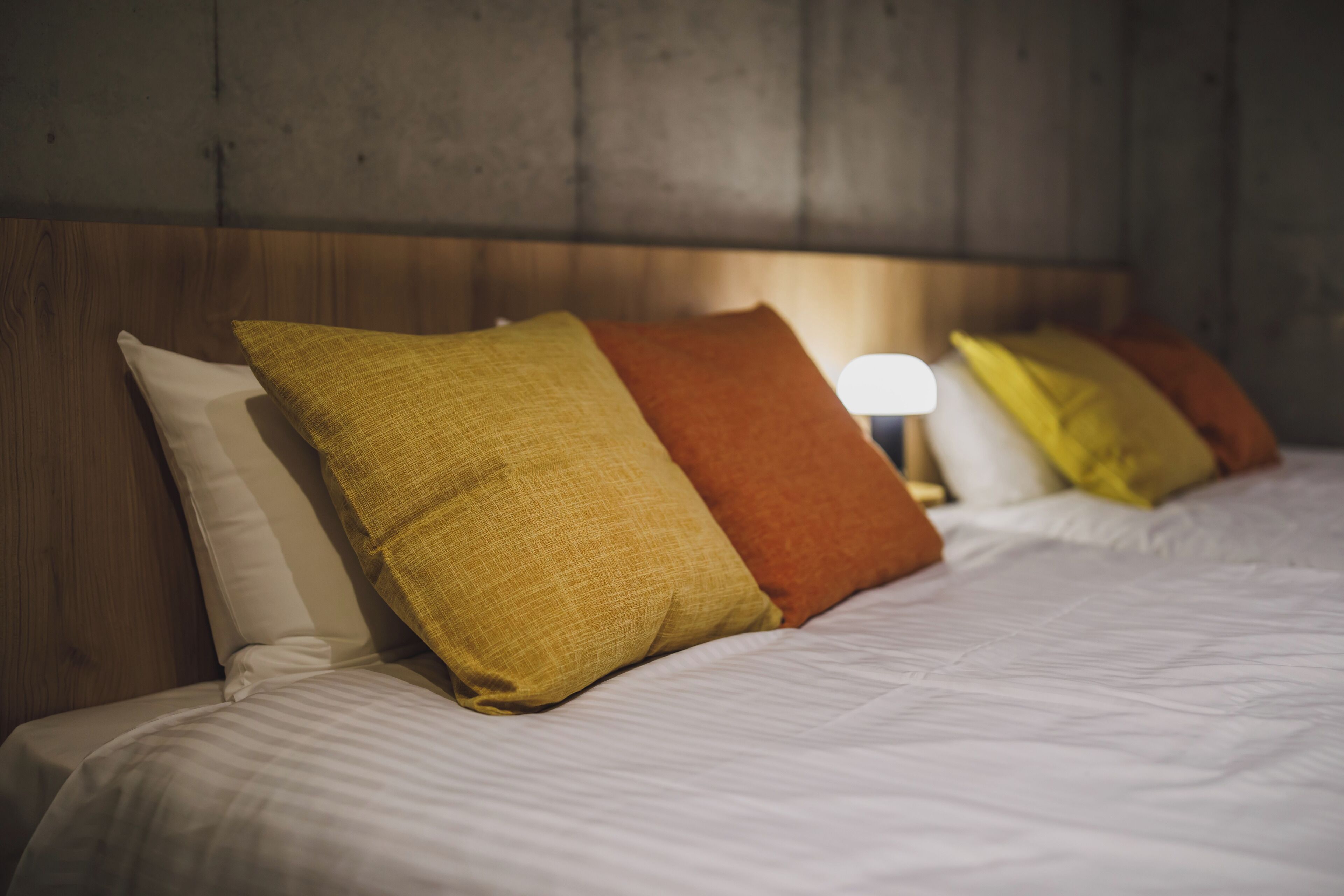 A neatly made bed with white bedding and three pillows in different colors.