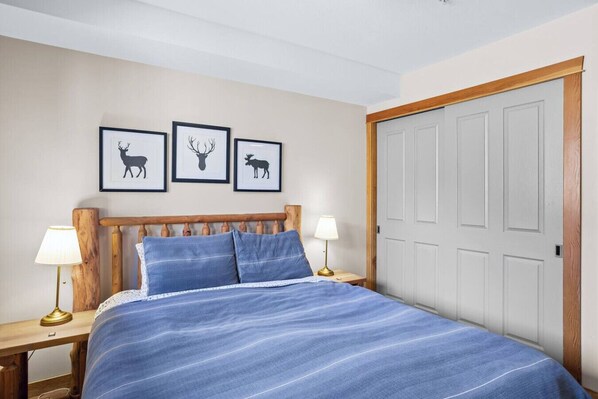 Un dormitorio con cabecera de madera, colcha a rayas azules, dos lámparas de noche y tres siluetas de animales enmarcadas en la pared.