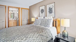 A bedroom with a patterned bedspread, two wall-mounted lamps, a wooden headboard, and two wall art pieces depicting nests.