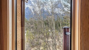 A window view of a mountainous landscape with bare trees and snow-capped peaks.