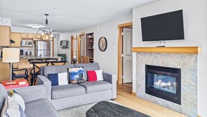 A modern living room with a fireplace, a flat-screen TV mounted above it, and a grey sofa with colorful cushions.