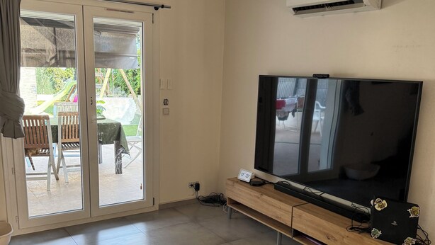 A living room with a TV on a wooden stand, a sliding glass door to a patio, and an air conditioning unit on the wall. - House 10 min from the sea With garden and swimming pool (Fréjus)