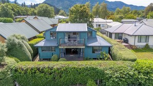 Una casa de dos pisos con balcón, rodeada de exuberante vegetación y montañas al fondo.