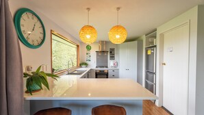 Una cocina moderna con una isla central, luces colgantes, un reloj y vistas a la vegetación.