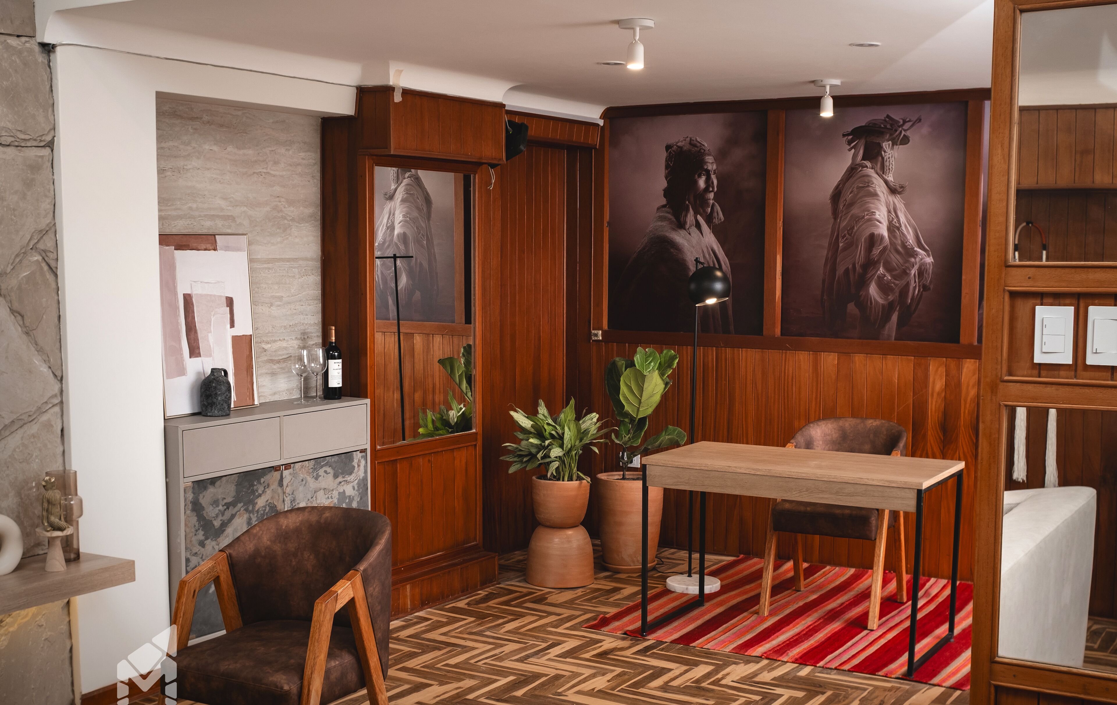 A modern interior with a wooden panel wall, a fireplace, a dining table with chairs, and large potted plants.