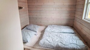 Een kleine kamer met een enkel bed, een houten spilplafond en een raam aan de rechterkant.