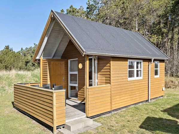 Une petite cabane en bois, dotée d’un toit en pente, d’un porche à l’avant et d’une porte donnant sur l’intérieur.