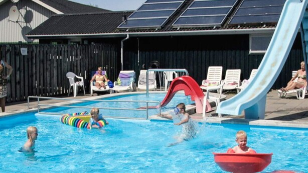 Een zwembad met meerdere glijbanen, ligbedden en een omheind gebied met zonnepanelen.