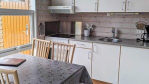 Een kleine keuken met witte kastjes, een zwart aanrecht en een raam met uitzicht op een houten terras.