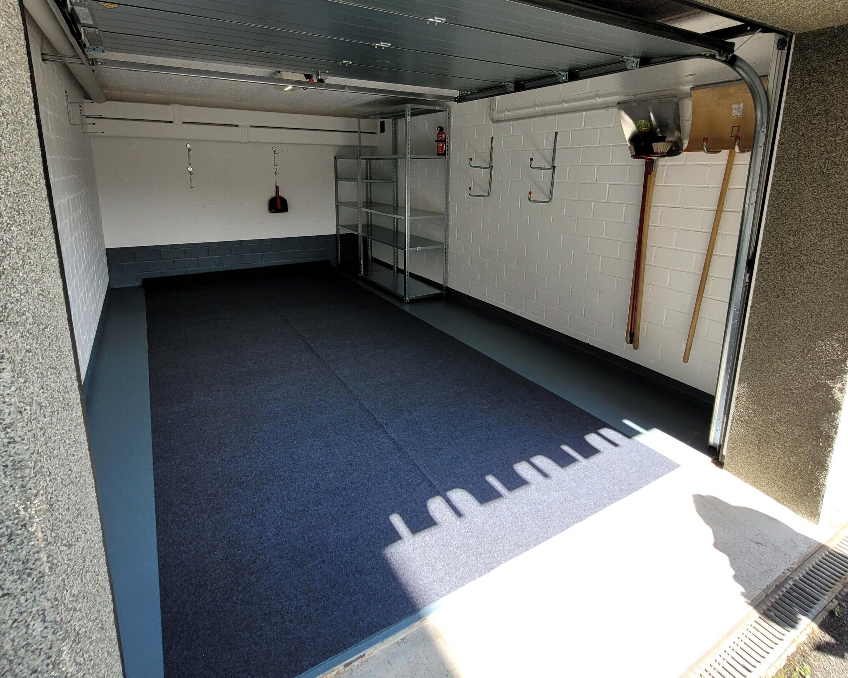 A clean, empty garage with a blue floor, white brick walls, and metal shelving units.