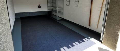 A clean, empty garage with a blue floor, white brick walls, and metal shelving units.