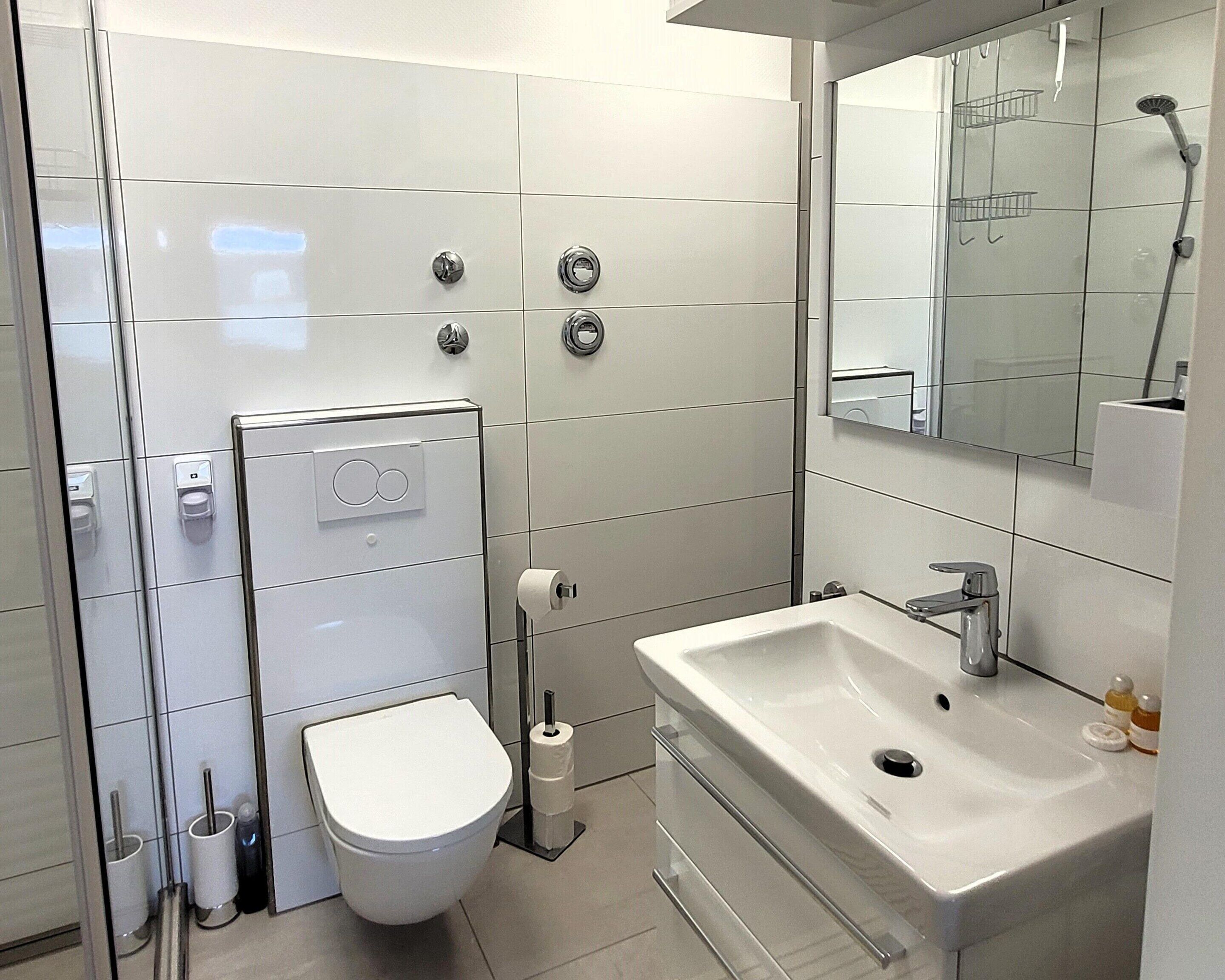 A modern bathroom with a toilet, bidet, sink, and mirror.