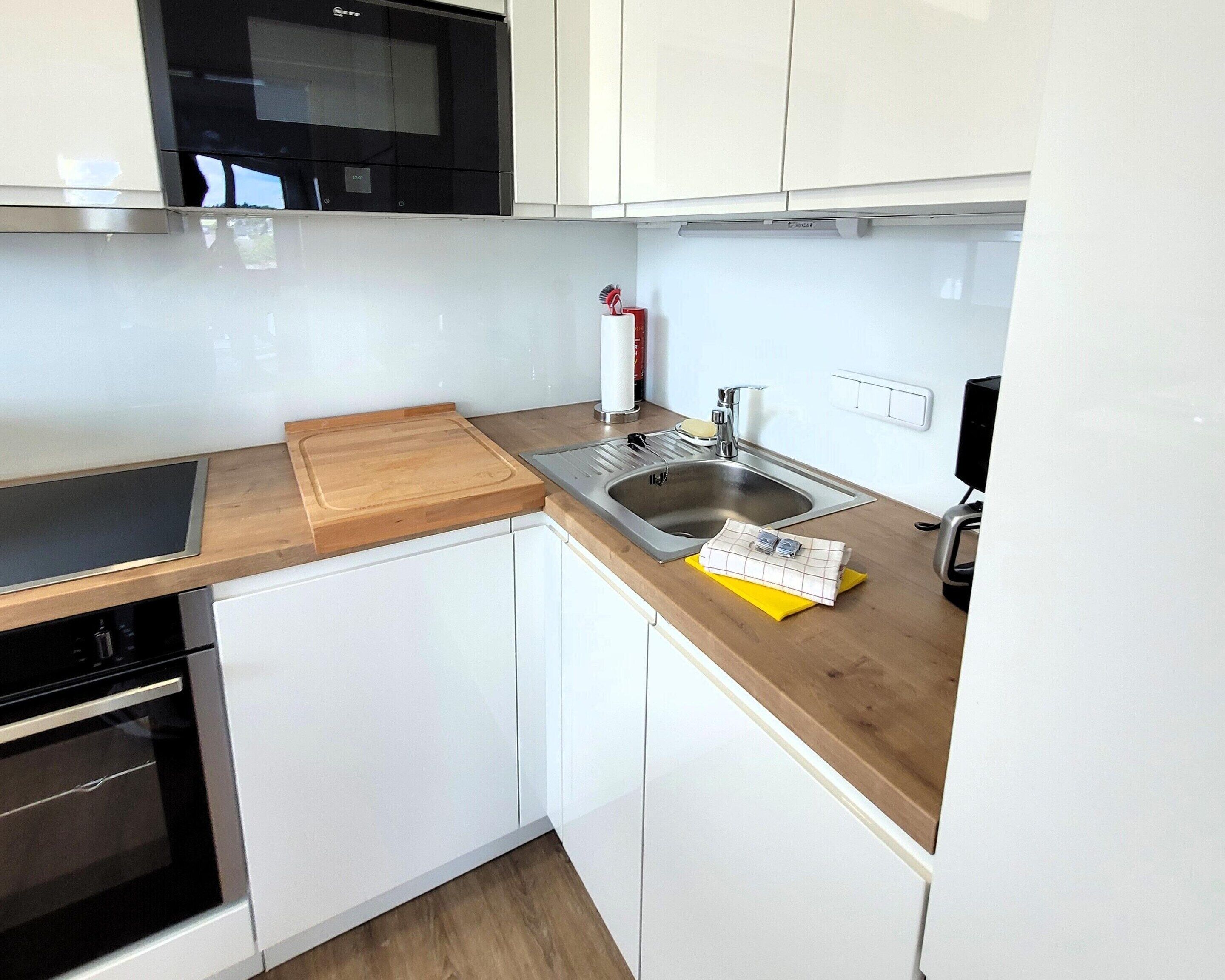 Une cuisine moderne avec des armoires blanches, un plan de travail en bois, un évier en acier inoxydable et un four à micro-ondes placé au-dessus de la cuisinière.