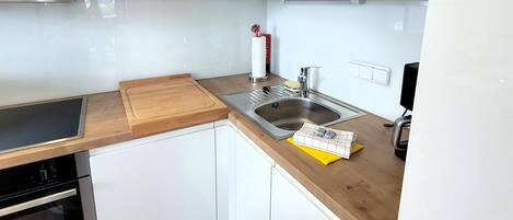 Une cuisine moderne avec des armoires blanches, un plan de travail en bois, un évier en acier inoxydable et un four à micro-ondes placé au-dessus de la cuisinière.