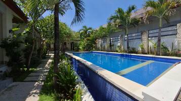 A swimming pool surrounded by palm trees and tropical plants, with a clear blue sky above.