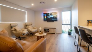 Ein modernes Wohnzimmer mit einer Couch, zwei Sesseln, einem Couchtisch und einem an der Wand befestigten Fernseher.