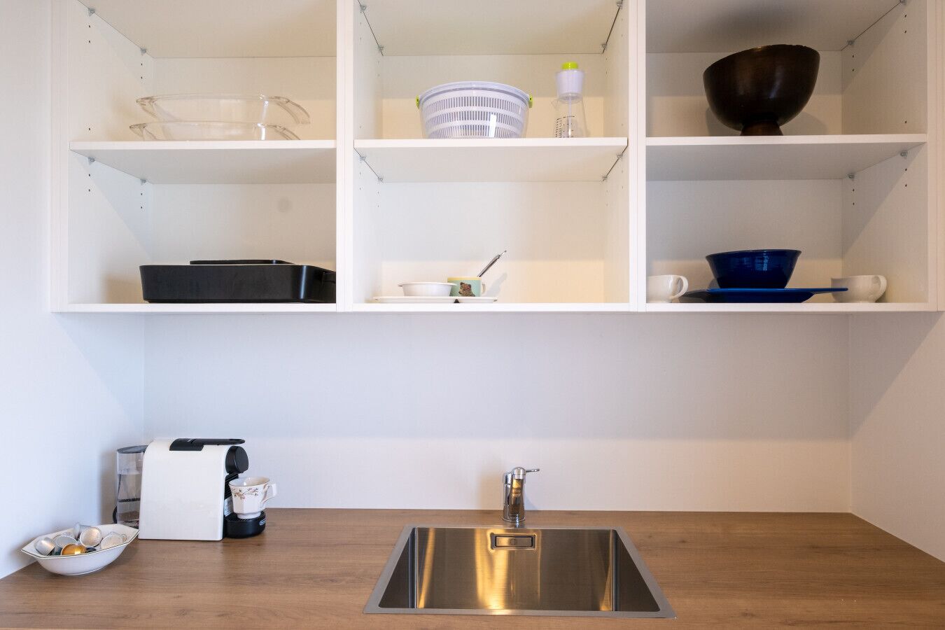 A kitchen with white shelves, a stainless steel sink, and various kitchen items.
