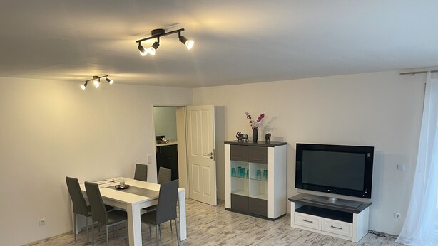 A modern living room with a dining area, a TV, and a cabinet with glass doors. - Spacious 80 m² vacation apartment with terrace for 4 people (Mörlenbach)