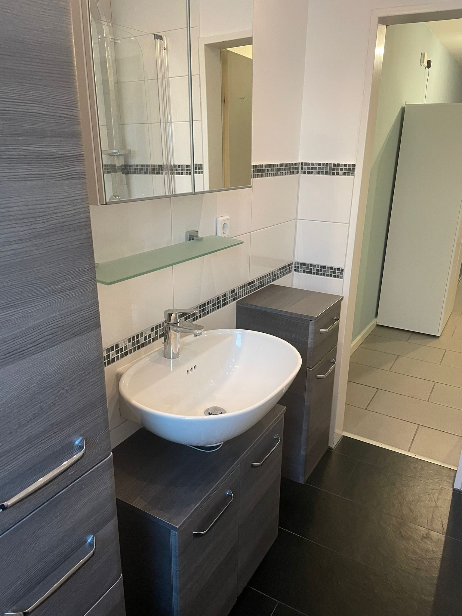 Een moderne badkamer met een witte wastafel, donker houten kastjes en een glazen plank.