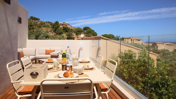 A balcony with a table set for breakfast, overlooking a scenic hillside. - Luxury apartment for 6 people, sea view, 800m from center and beaches (L'Île-Rousse)