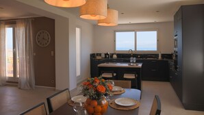 A modern kitchen with dark cabinetry, a central island, and a dining area with a table set for four. - Luxury apartment for 6 people, sea view, 800m from center and beaches (L'Île-Rousse)