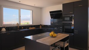 A modern kitchen with dark cabinetry, a large island, and a view of the outdoors. - Luxury apartment for 6 people, sea view, 800m from center and beaches (L'Île-Rousse)