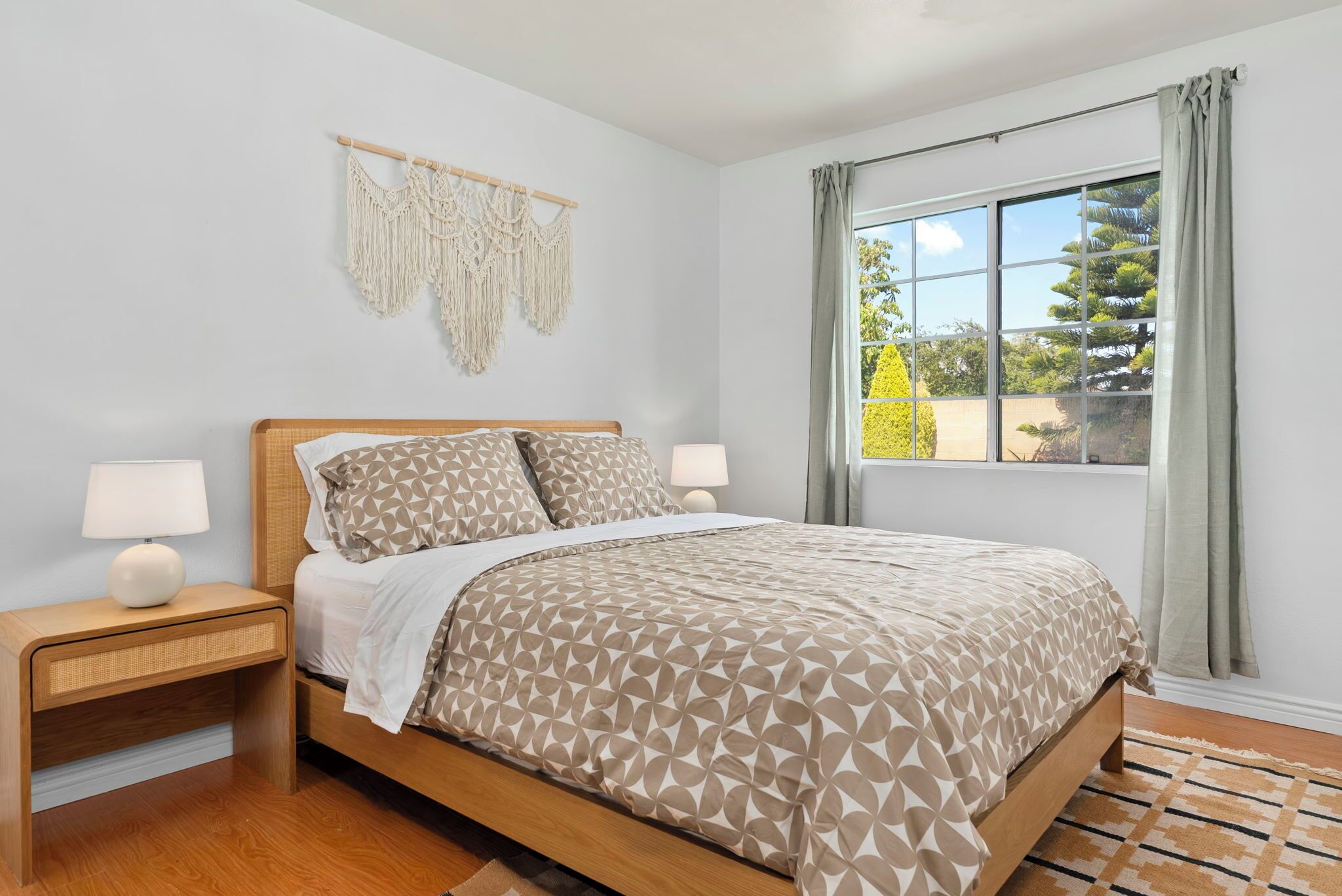 A bedroom with a bed, nightstands, a macrame wall hanging, and a window with curtains.