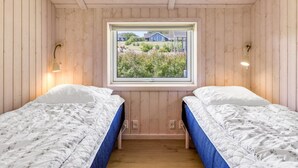 Ein kleiner Raum mit Holzwandverkleidung, zwei Betten, einem Fenster mit Blick auf einen Garten und Häuser sowie Wandleuchten.