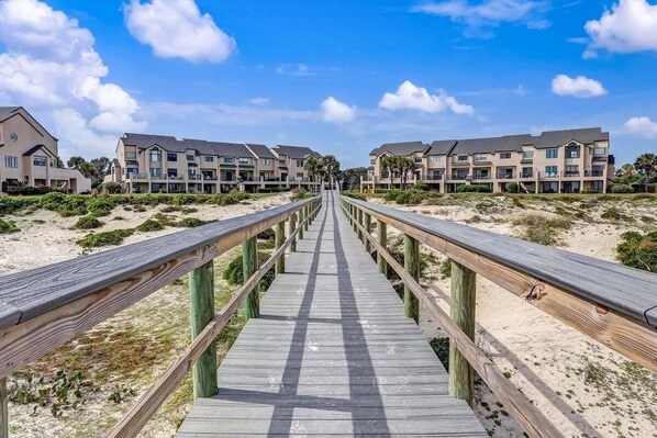 Un muelle de madera que conduce a un hotel frente al mar con edificios de varios pisos.