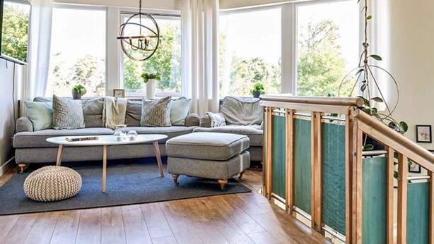 Een moderne woonkamer met een grijze bank, een ronde salontafel en een houten trap.
