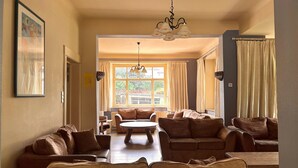 A spacious living area with multiple sofas and a coffee table, a chandelier, and a large window with curtains. - Group Home in La Roche With Sauna (La Roche-en-Ardenne)