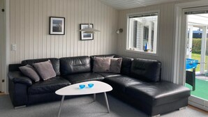 A modern living room with a black leather sectional sofa, a white coffee table, and a large window with a view of the outdoors.