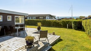A wooden deck with outdoor furniture, a grassy lawn, and a view of the sea.