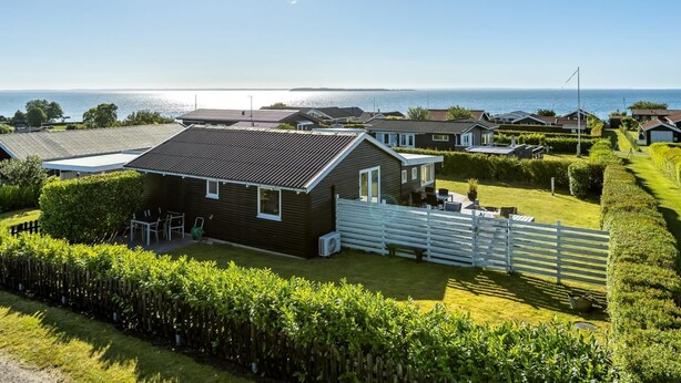 A coastal residential area with houses, a grassy lawn, and a view of the sea.
